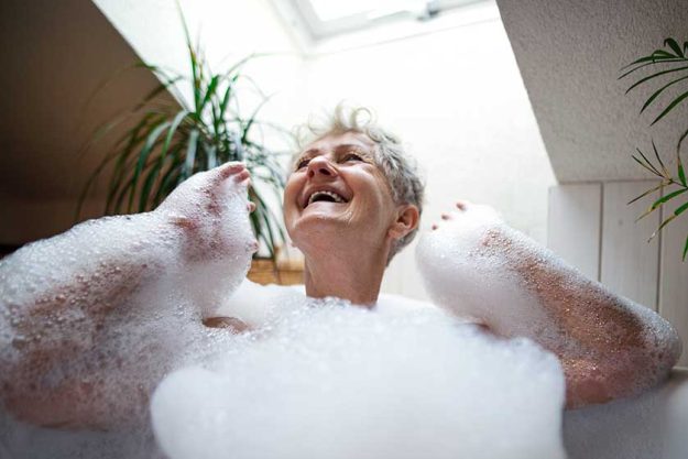 Cheerful senior woman washing in bubble bath tub at home, laughing. Cheerful senior woman washing in bubble bath tub at home, laughing.