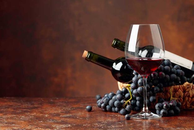 Juicy blue grapes and bottles of red wine on a brown background. Juicy blue grapes and bottles of red wine on a brown background.