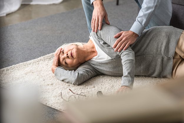 cropped view of man helping senior mother with heart attack fallen on carpet