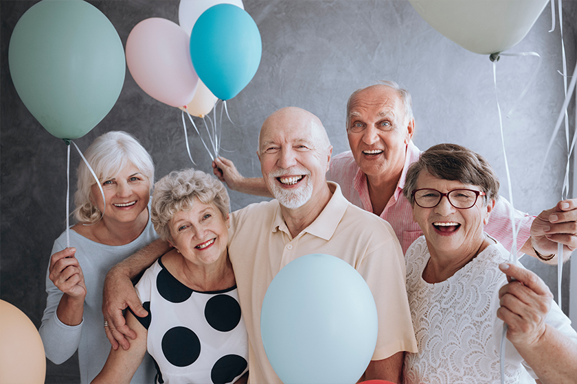 Smiling senior friends with colorful balloons enjoying meeting