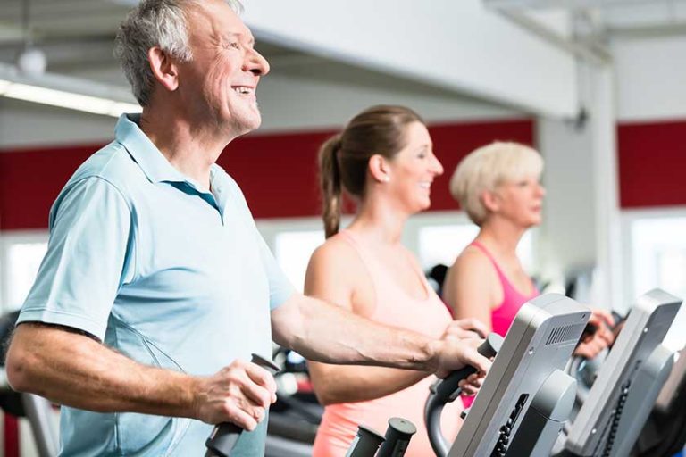 Happy seniors train on cross trainer with personal trainer at the gym