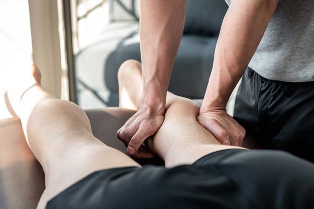 Male therapist giving leg and calf massage to athlete patient