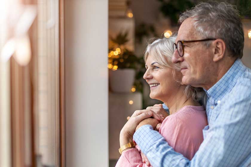 Mature couple looking out through window at home Mature couple looking out through window at home