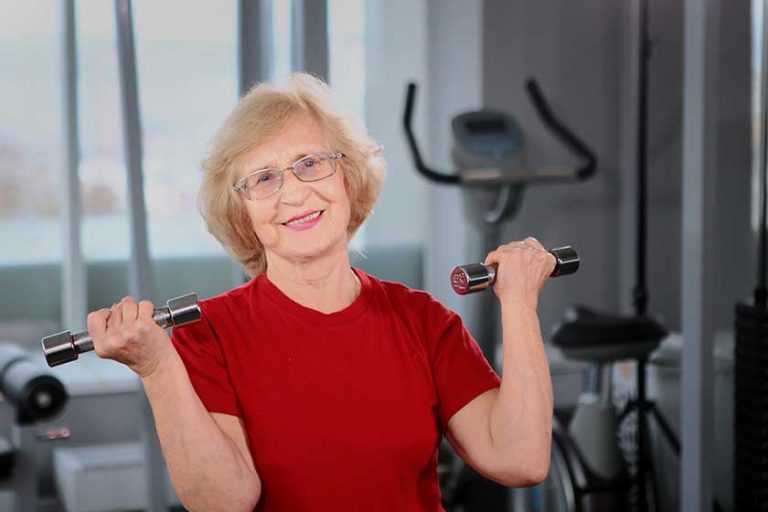 An elderly woman holds dumbbells in her hands