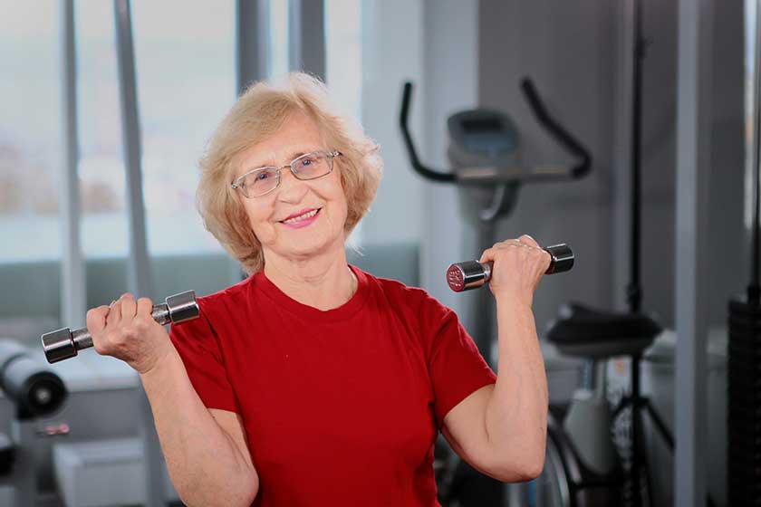 An elderly woman holds dumbbells in her hands