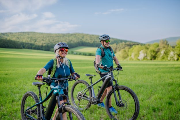 Active senior couple with electric bicycles on meadow in summer, healthy lifestyle concept. Active senior couple with electric bicycles on meadow in summer, healthy lifestyle concept.