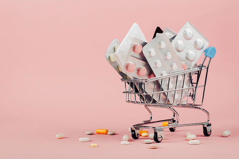 Shopping cart loaded with pills on a pink background
