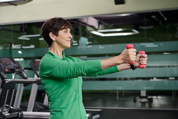 Happy woman with short hair working out with dumbbells in gym, active senior, healthy lifestyle