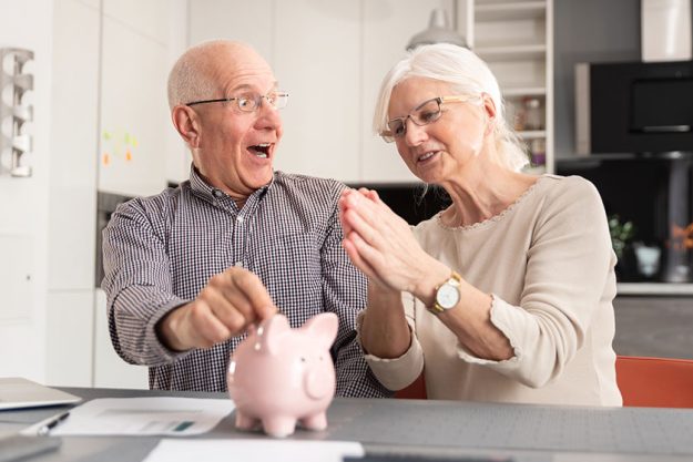 Senior couple putting coin into piggy bank