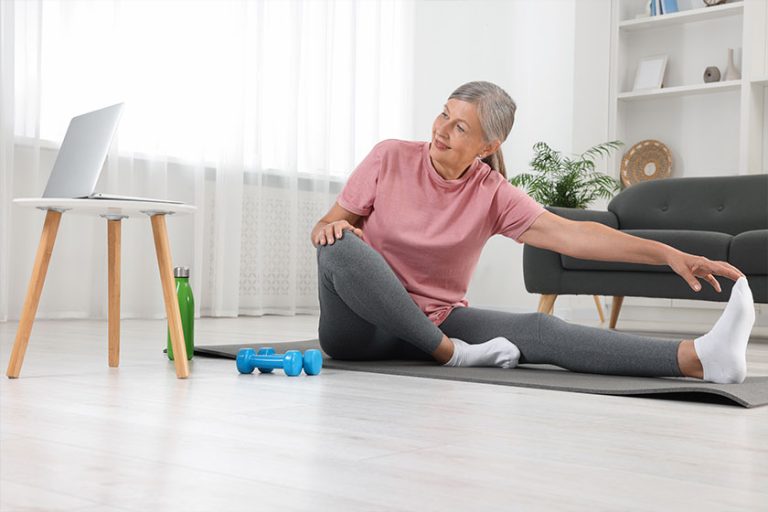 Senior woman in sportswear stretching on fitness mat home