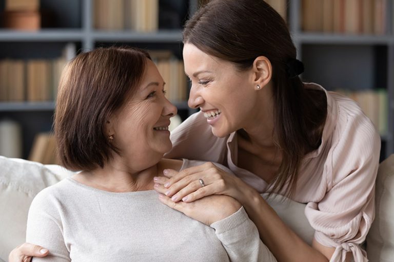 Young woman embracing from back sitting on sofa older mother.