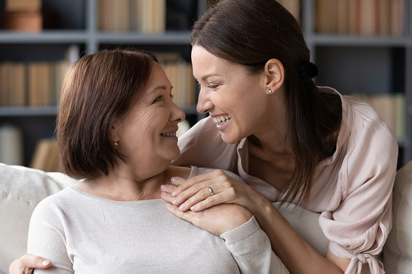 Young woman embracing from back sitting on sofa older mother. Young woman embracing from back sitting on sofa older mother.