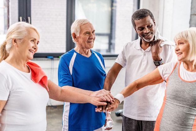Positive multiculutral senior sportspeople putting hands together at sports hall