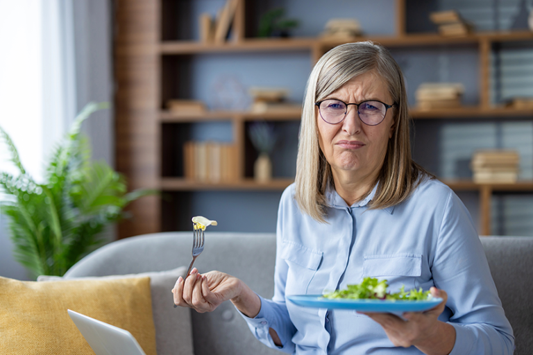Senior woman in glasses holds plate of salad