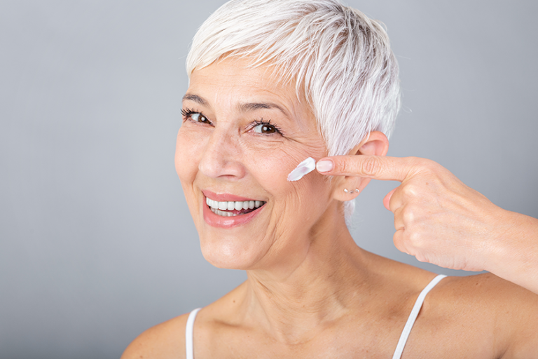 Smiling senior woman applying anti-aging lotion