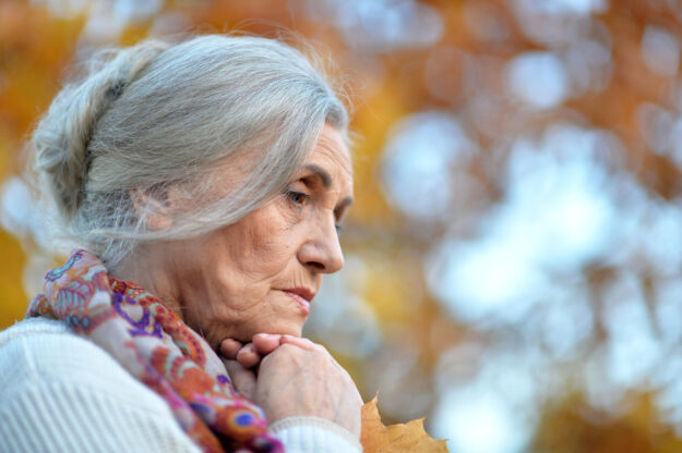Portrait of beautiful sad senior woman on blurred autumn background