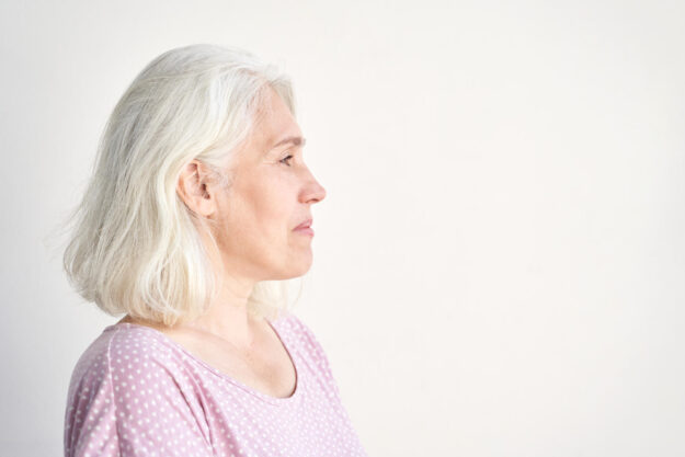 Profile of a contemplative elderly woman with gray hair in casual attire against